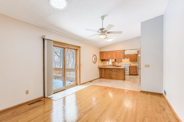 unfurnished living room with ceiling fan, vaulted ceiling, a textured ceiling, and light wood-type flooring