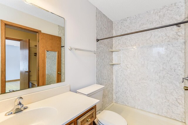 bathroom with tiled shower, vanity, toilet, and a textured ceiling