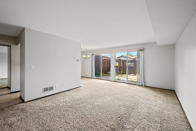 carpeted empty room featuring a textured ceiling and an inviting chandelier