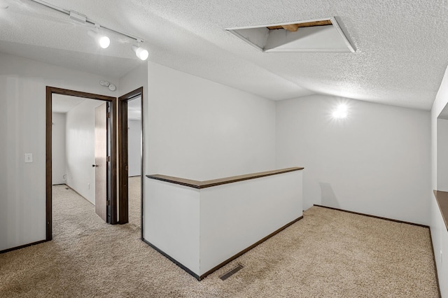 hall with vaulted ceiling, light colored carpet, and a textured ceiling