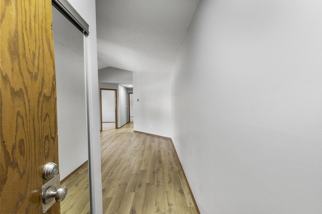 corridor featuring vaulted ceiling, a textured ceiling, and light hardwood / wood-style floors