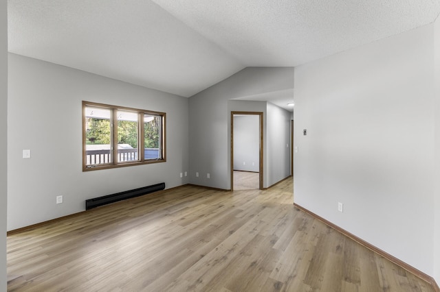 empty room featuring a baseboard heating unit, vaulted ceiling, a textured ceiling, and light wood-type flooring