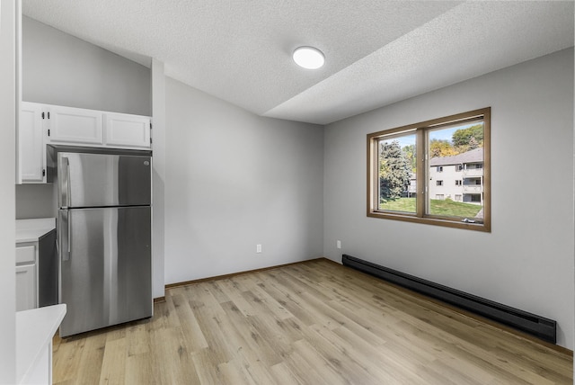 kitchen featuring white cabinets, stainless steel fridge, a baseboard heating unit, light hardwood / wood-style floors, and a textured ceiling