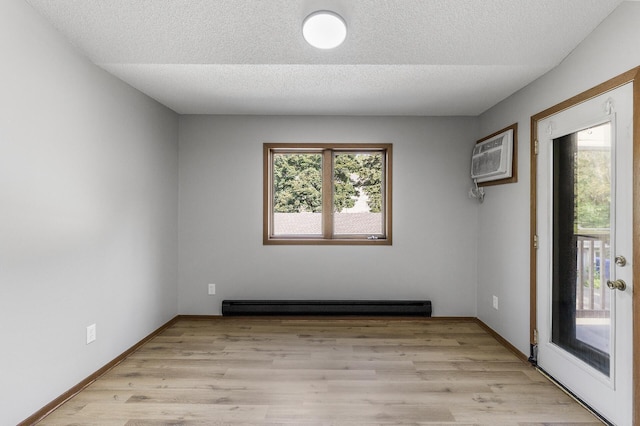 spare room featuring a baseboard heating unit, a wall unit AC, a textured ceiling, and light hardwood / wood-style floors