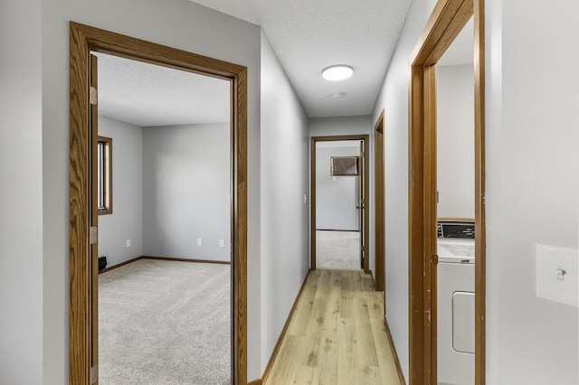 hallway featuring washer / dryer, light carpet, and a textured ceiling