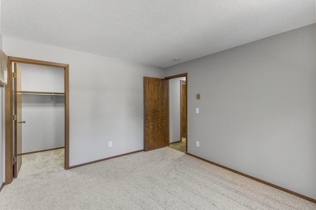 unfurnished bedroom with a walk in closet, light carpet, and a textured ceiling