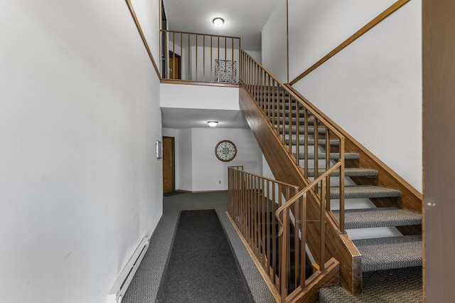 staircase featuring carpet, a baseboard heating unit, and a towering ceiling