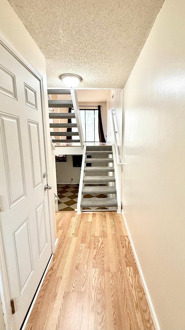 stairway featuring wood finished floors, baseboards, and a textured ceiling