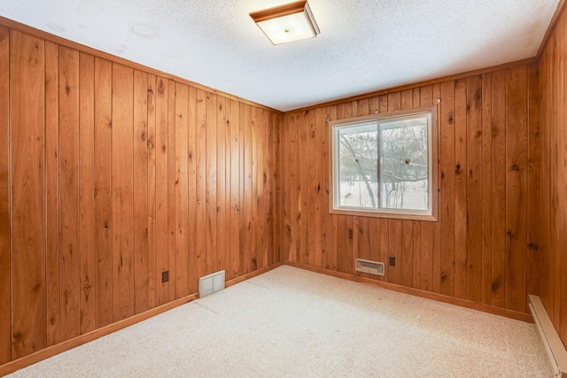 carpeted spare room with wood walls, a textured ceiling, and baseboard heating