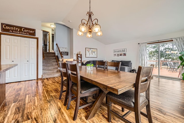 dining room with lofted ceiling, a notable chandelier, wood finished floors, and stairs