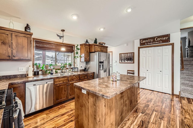 kitchen with a sink, a kitchen island, dark countertops, light wood-style floors, and appliances with stainless steel finishes