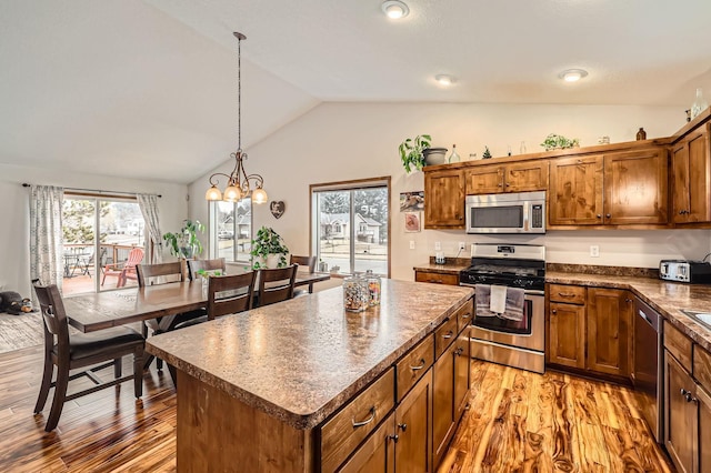 kitchen featuring stainless steel appliances, vaulted ceiling, light wood-style floors, dark countertops, and brown cabinets