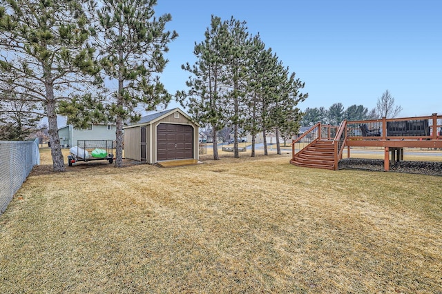 view of yard featuring fence, a wooden deck, a garage, an outdoor structure, and driveway