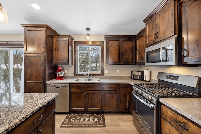 kitchen with sink, light stone counters, decorative light fixtures, light hardwood / wood-style flooring, and stainless steel appliances