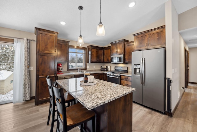 kitchen featuring appliances with stainless steel finishes, decorative light fixtures, a center island, light hardwood / wood-style floors, and light stone countertops