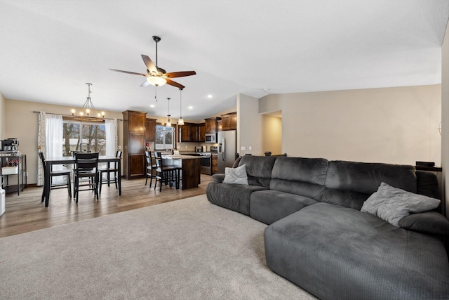 living room featuring ceiling fan with notable chandelier, vaulted ceiling, and light wood-type flooring