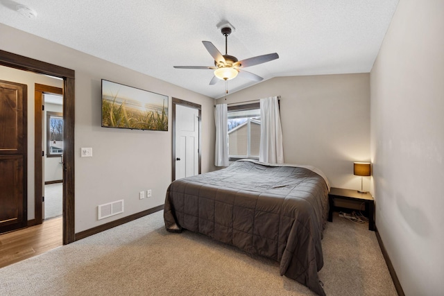 bedroom with lofted ceiling, ceiling fan, light colored carpet, and a textured ceiling