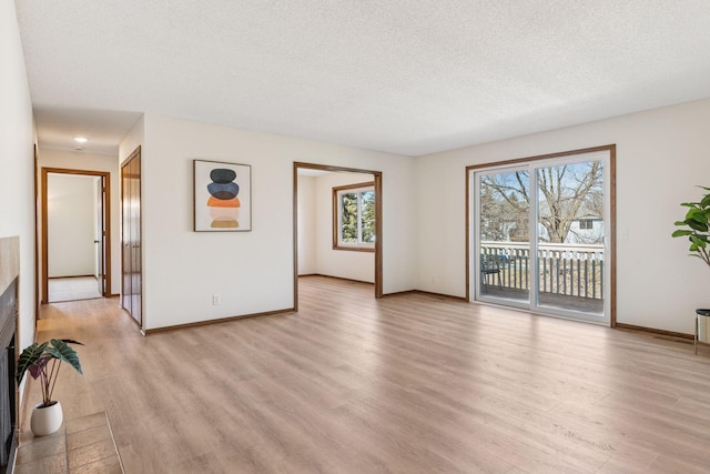 unfurnished living room featuring baseboards, a fireplace with flush hearth, a textured ceiling, and light wood-style flooring