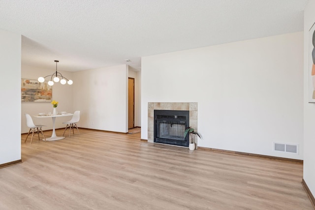 unfurnished living room featuring light wood-type flooring, visible vents, a textured ceiling, and a tile fireplace