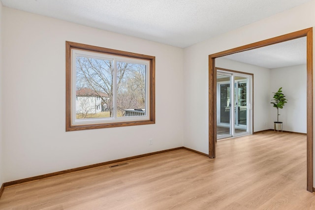 spare room featuring a textured ceiling, baseboards, visible vents, and light wood-type flooring