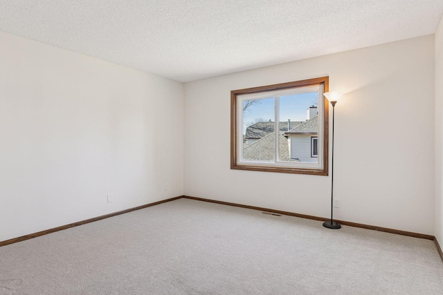 empty room with a textured ceiling, light colored carpet, visible vents, and baseboards