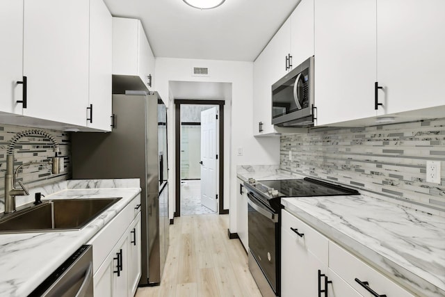 kitchen featuring white cabinetry, sink, light hardwood / wood-style floors, stainless steel appliances, and light stone countertops