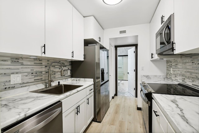 kitchen with sink, white cabinetry, light stone counters, stainless steel appliances, and light hardwood / wood-style floors