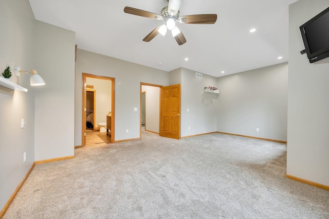 unfurnished bedroom with ensuite bathroom, a walk in closet, light colored carpet, and ceiling fan