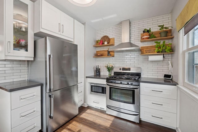 kitchen featuring wall chimney range hood, white cabinetry, stainless steel appliances, dark hardwood / wood-style floors, and decorative backsplash