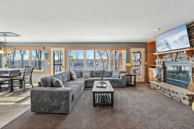 living room featuring a textured ceiling, a stone fireplace, dark colored carpet, and a wealth of natural light