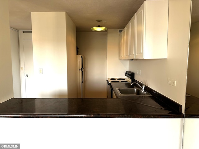kitchen with freestanding refrigerator, range with electric stovetop, dark countertops, and a sink