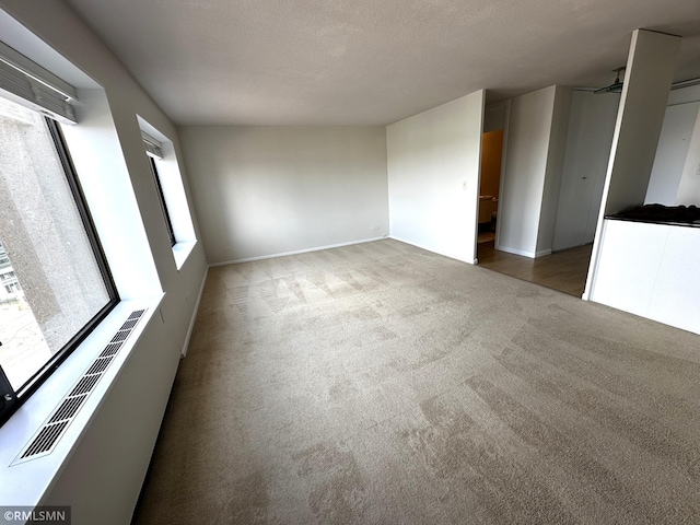 carpeted spare room with a textured ceiling, visible vents, and baseboards