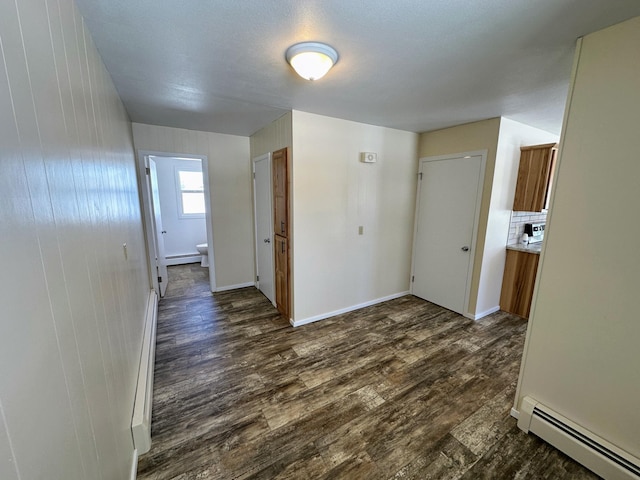 corridor featuring baseboards, baseboard heating, and dark wood finished floors