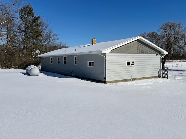 snow covered rear of property with a chimney