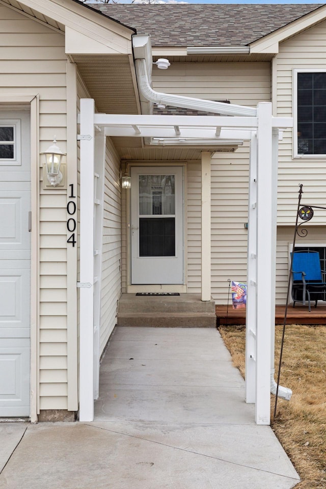 entrance to property with a garage and a shingled roof