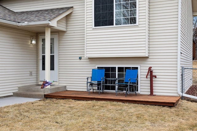 doorway to property featuring a shingled roof, a lawn, and a wooden deck