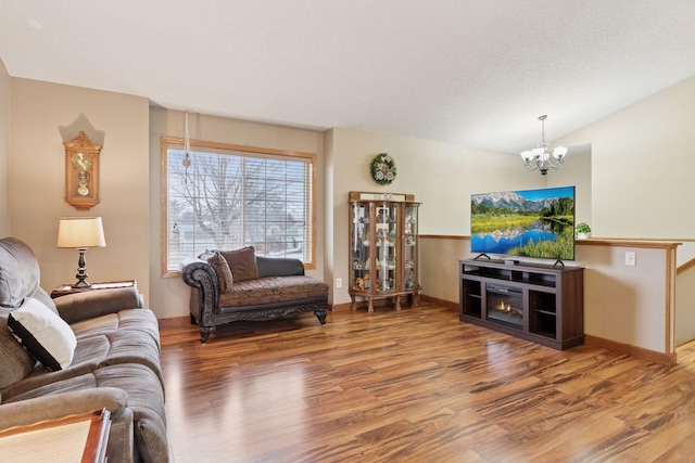 living room with an inviting chandelier, vaulted ceiling, a textured ceiling, wood finished floors, and baseboards