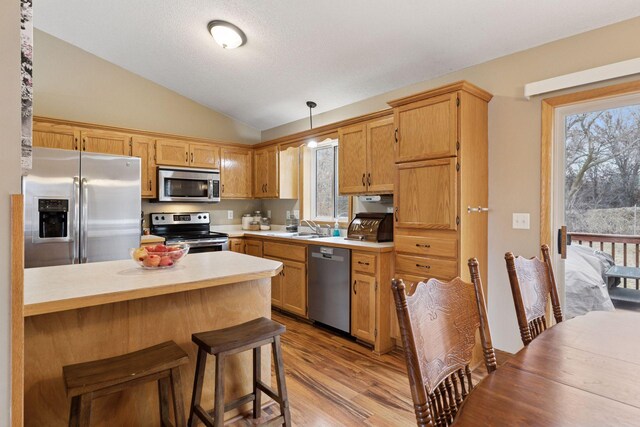 kitchen featuring appliances with stainless steel finishes, wood finished floors, a peninsula, vaulted ceiling, and light countertops