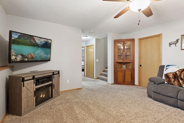 living area with a ceiling fan, carpet flooring, a textured ceiling, baseboards, and stairs