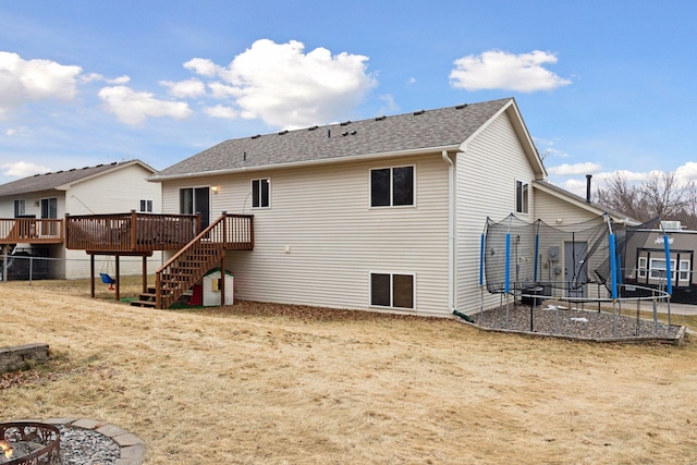 back of house featuring a trampoline, roof with shingles, a fire pit, a wooden deck, and stairs