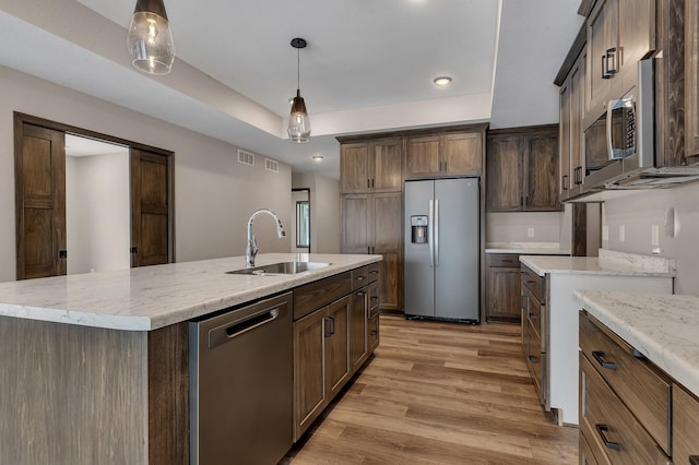 kitchen with sink, hanging light fixtures, light wood-type flooring, an island with sink, and stainless steel appliances