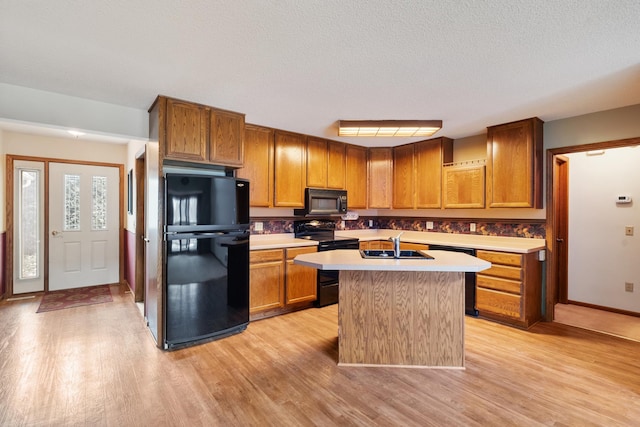 kitchen featuring light wood-style floors, an island with sink, light countertops, black appliances, and a sink