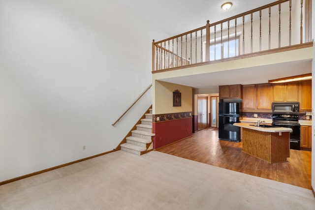 kitchen featuring a center island with sink, baseboards, light colored carpet, a high ceiling, and black appliances