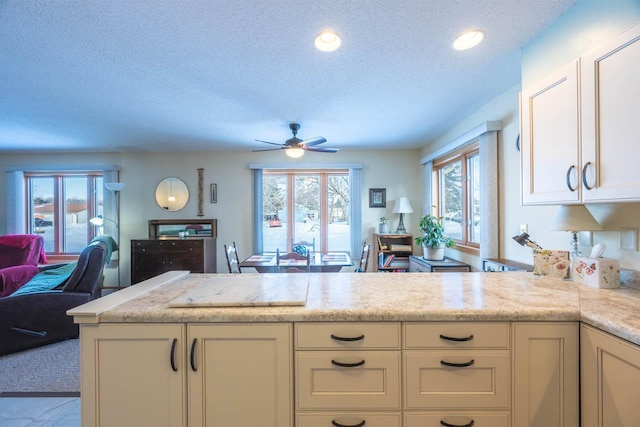 kitchen featuring ceiling fan, light stone countertops, a textured ceiling, and kitchen peninsula