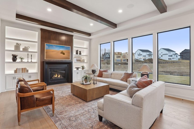 living room with beamed ceiling, a fireplace, built in shelves, and light wood-type flooring