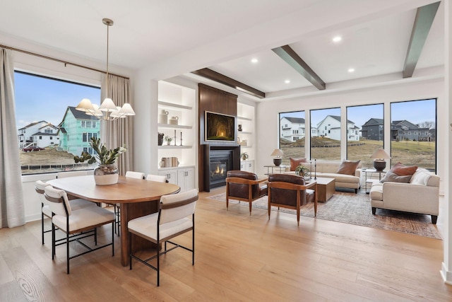 dining space with beam ceiling, a wealth of natural light, a fireplace, and light hardwood / wood-style floors