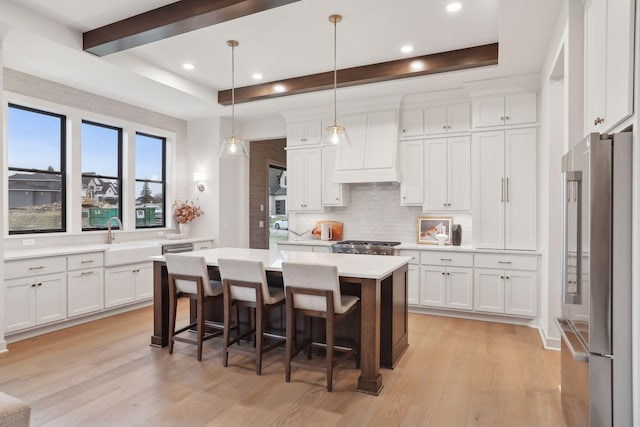 kitchen with sink, white cabinetry, high end refrigerator, decorative light fixtures, and a center island