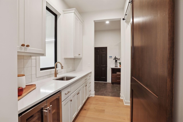 kitchen featuring sink, white cabinets, a barn door, light hardwood / wood-style floors, and backsplash