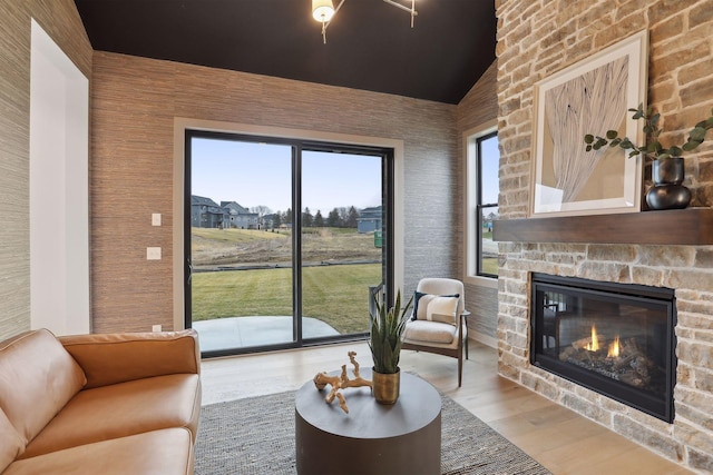 living room featuring lofted ceiling, a stone fireplace, and light wood-type flooring