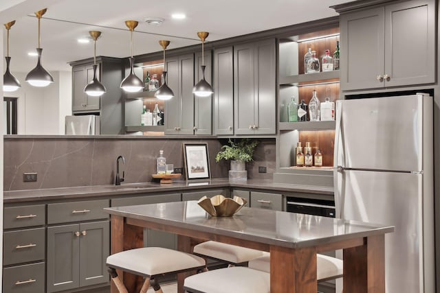 kitchen with sink, gray cabinetry, hanging light fixtures, stainless steel refrigerator, and decorative backsplash